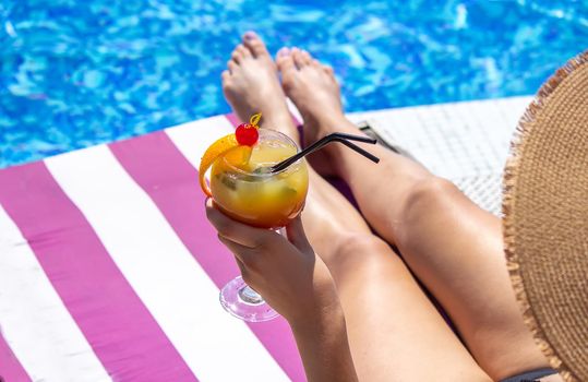 a girl on a sun lounger near the pool drinks a cocktail from a freshly squeezed orange.