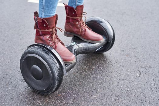 Woman using hoverboard on asphalt road, close up. Feet on electrical scooter outdoor