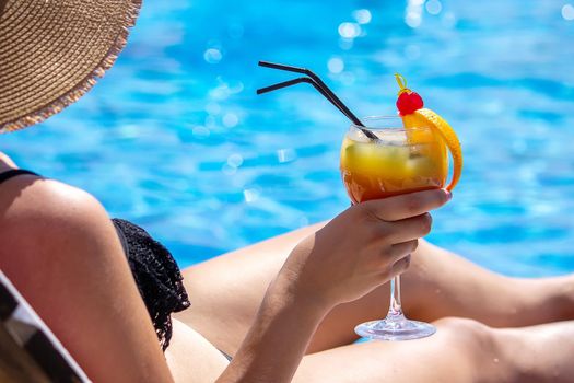 a girl on a sun lounger near the pool drinks a cocktail from a freshly squeezed orange.