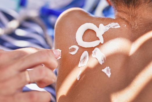 Woman apply protective sunscreen on boy's shoulders skin