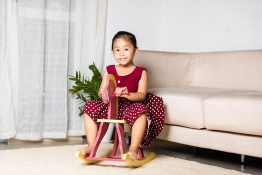 Asian cute little girl swinging riding toy horse, Smiling kid playing horse rocking chair at home in living room, Happy time to play during self kindergarten preschool