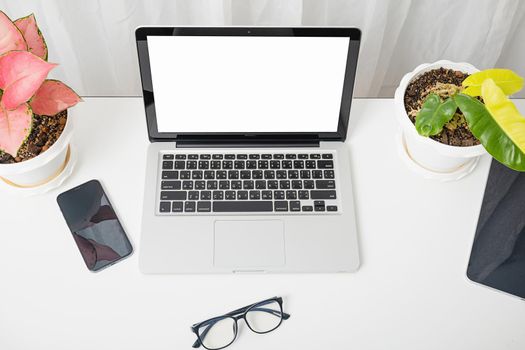 Modern workspace, mock up laptop computer blank white screen, eyeglasses and smartphone white table have potted plants on the desk, Notebook and mobile phone on desktop home office