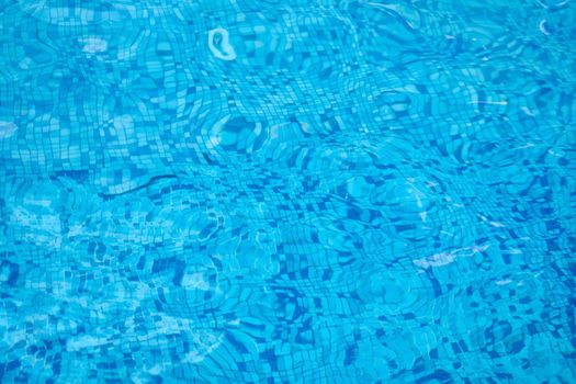 Background of water in blue swimming pool, water surface with sun reflection