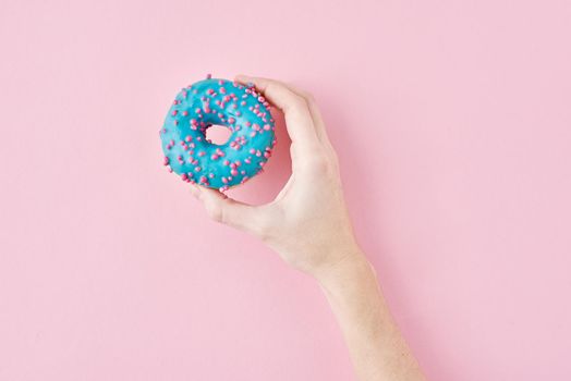 Woman hand take color donut on pink background. Creativity minimalism style food concept, top view