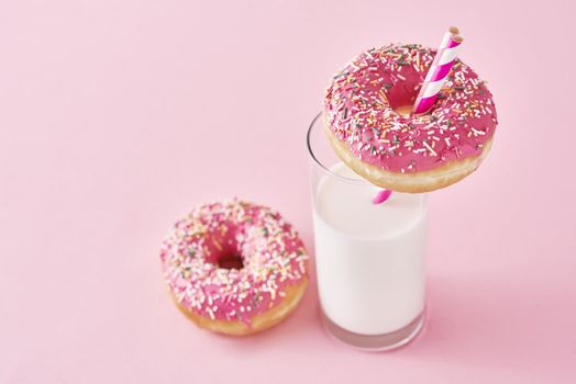 Donuts decorated with icing and sprinkle and glass of milk on pink background