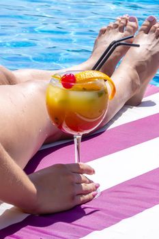 a girl on a sun lounger near the pool drinks a cocktail from a freshly squeezed orange.