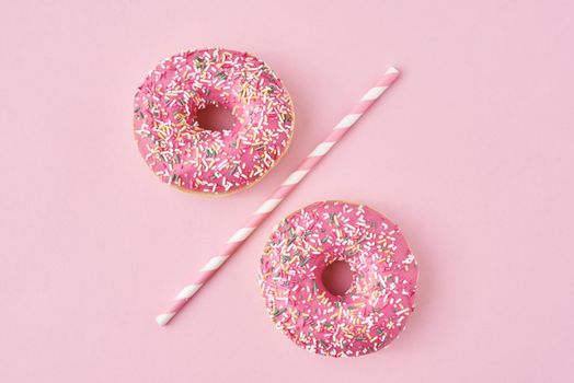 Two donuts separated with drinking straw on pink background. Creative food concept