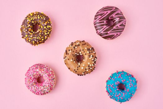 Different types of colorful donats decorated sprinkles and icing on pastel pink background