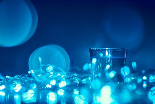 Silhouette of burning candle with golden blurred lights on dark background, blue toned photo