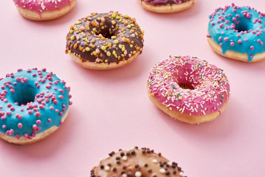 Pattern with different types of colorful donats decorated sprinkles and icing on pastel pink background, top view flat lay