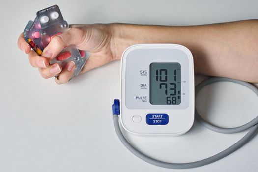 hand with a handful of pills and digital blood pressure monitor . Healthcare and medicine concept