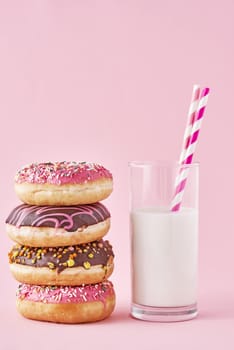 Stack of colorful donuts decorated and glass of milk on pink background