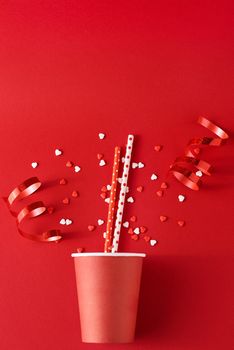 Paper coffee cup with festive decorations and confetti on red backgrond, top view flat lay. Creative minimalism concept