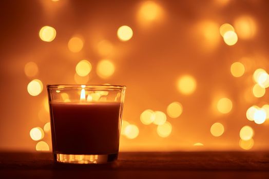 Silhouette of burning candle with golden blurred lights on dark background