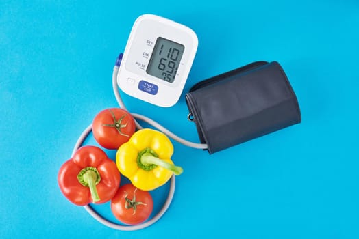 Digital blood pressure monitor and fresh vegetables on blue background. Healthcare concept