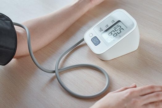 Woman measuring blood pressure with digital pressure monitor against blue background. Health care and medical concept