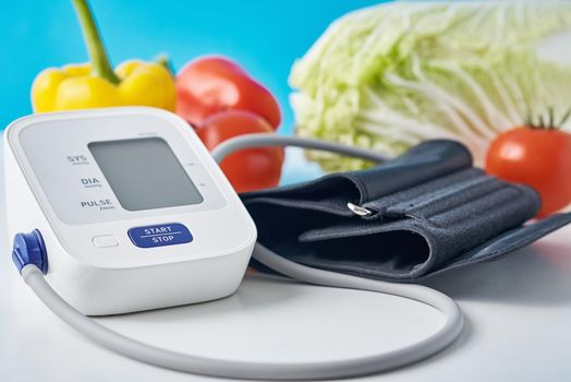 Digital blood pressure monitor and fresh vegetables on table against blue background. Healthcare concept