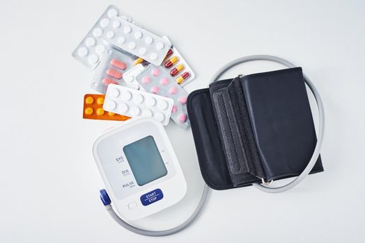 Digital blood pressure monitor and medical pills on white table. Healthcare and medicine concept