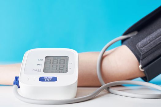 Woman measuring blood pressure with digital pressure monitor against blue background. Health care and medical concept