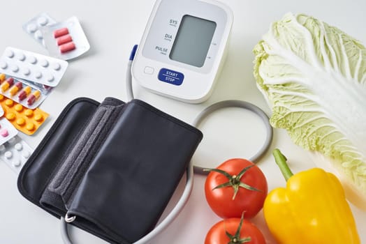 Digital blood pressure monitor, fresh vegetables and medical pills on white background. Healthy lifestyle concept