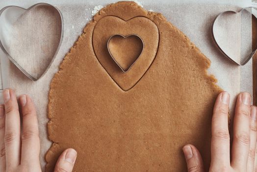 Making gingerbread cookies in shape of a heart for Valentines Day. Woman hand use cookie cutter. Holiday food concept