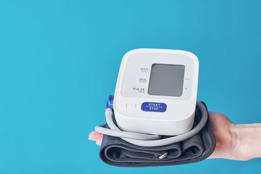 Digital blood pressure on hand against blue background with copy space. Healthcare and medicine concept