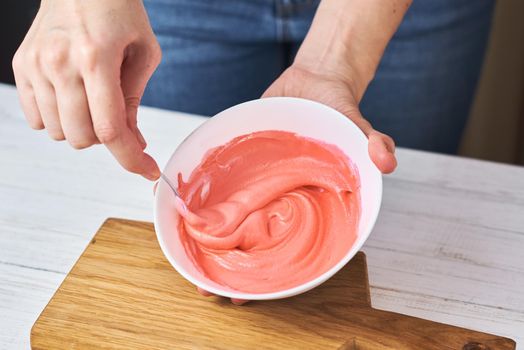 Woman whisking red cream for decorating cookies in bowl on kitchen, closeup