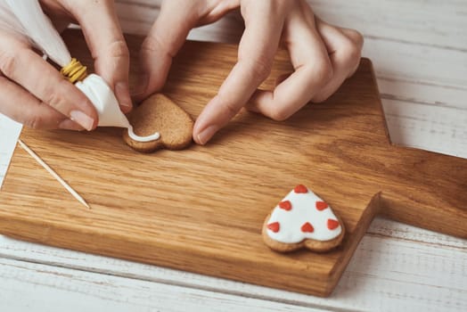 Decorating gingerbread cookies with icing. Woman hands decorate cookies in shape of heart, closeup