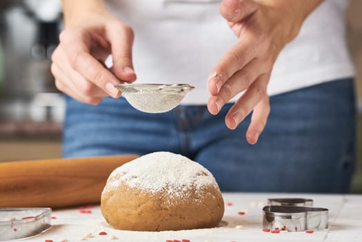 Woman sprinkling flour over fresh dough on kitchen table
