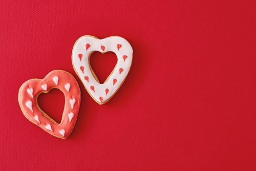 Two decorated with icing and glazed heart shape cookies on red background with copy space. Valentines Day food concept