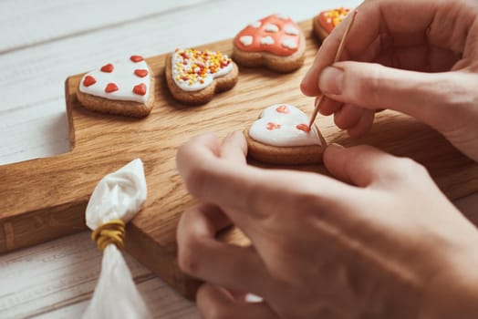 Decorating gingerbread cookies with icing. Woman hands decorate cookies in shape of heart, closeup