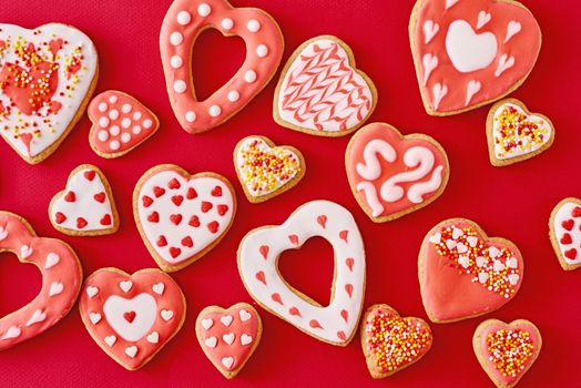 Background of decorated with icing and glazed heart shape cookies on red background, flat lay. Valentines Day food concept