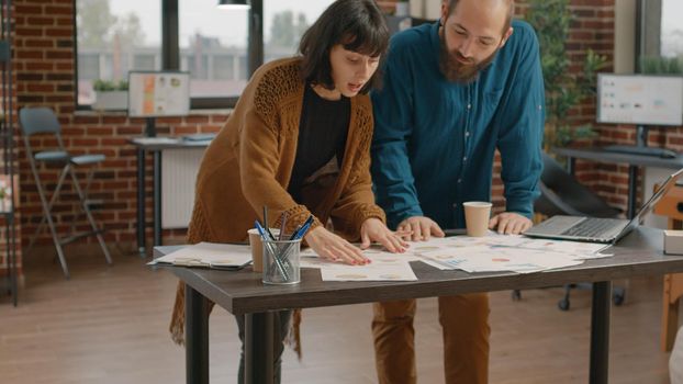 Colleagues having discussion about project planning and marketing strategy, working together on business. Man and woman doing teamwork with laptop and papers to design presentation.