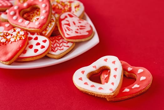 Decorated heart shape cookies in white plate and two cookies on red background. Valentines Day food concept