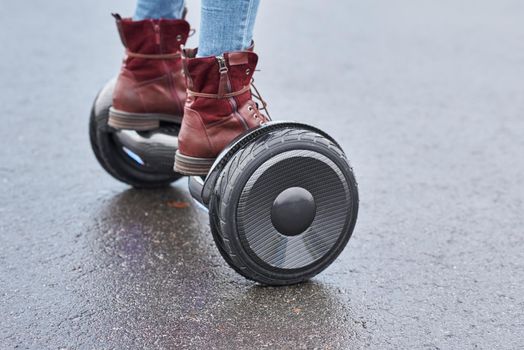 Woman using hoverboard on asphalt road, close up. Feet on electrical scooter outdoor