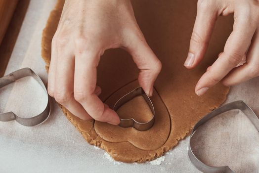 Making gingerbread cookies in shape of a heart for Valentines Day. Woman hand use cookie cutter. Holiday food concept