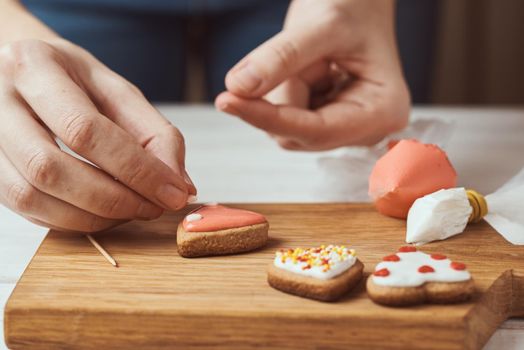 Decorating gingerbread cookies with icing. Woman hands decorate cookies in shape of heart, closeup