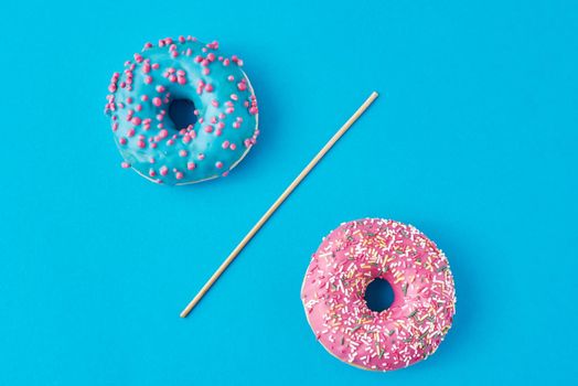 Two donuts separated with drinking straw on blue background. Creative food concept