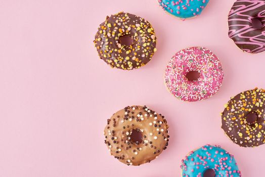 Pattern with different types of colorful donats decorated sprinkles and icing on pastel pink background, top view flat lay