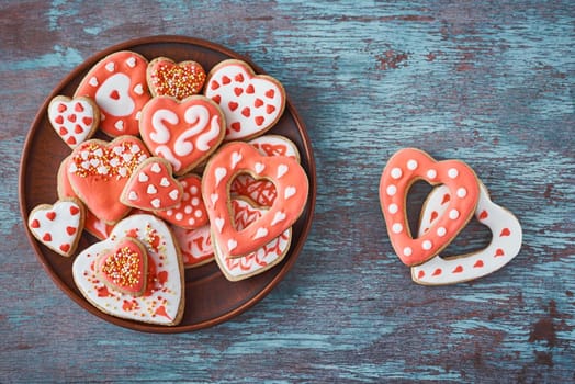 Decorated heart shape cookies in white plate and two cookies on gray background, top view. Valentines Day food concept