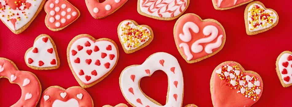 Background of decorated with icing and glazed heart shape cookies on red background, long banner. Valentines Day food concept