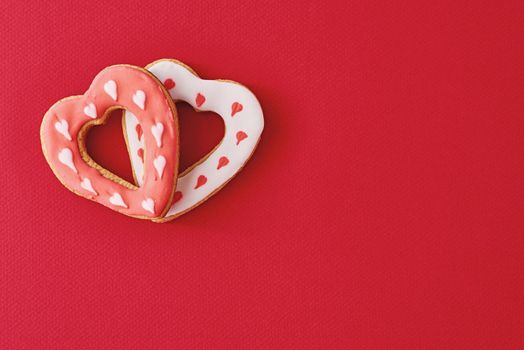 Two decorated with icing and glazed heart shape cookies on red background with copy space. Valentines Day food concept