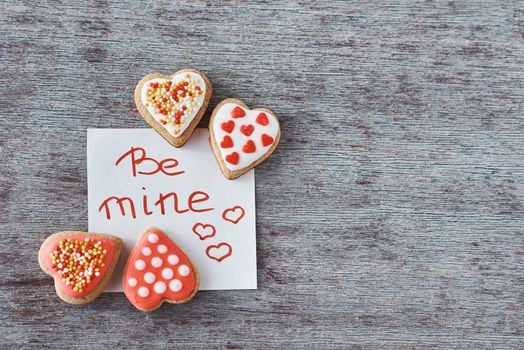 Deocrated heart shape cookies and paper sheet with inscription be mine on gray background. Valentines Day concept