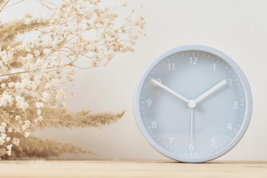 Alarm clock and homemade vase with dries plant on wooden table