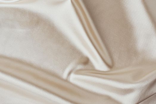 Golden light silk background with folds. Abstract texture of rippled satin surface