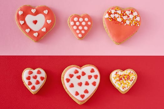 Decorated heart shape cookies on colored red and pink background, top view