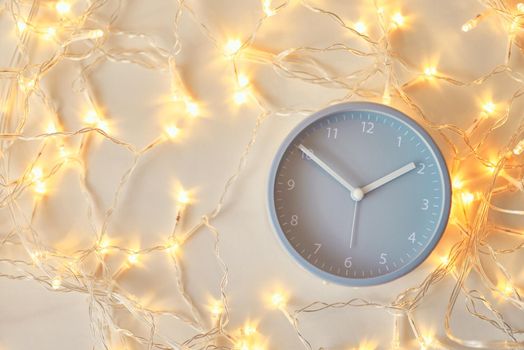 Classic alarm clock and garland lights on white background, top view