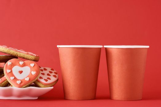 Decorated heart shape cookies and two paper coffee cups on red background. Valentines Day food concept