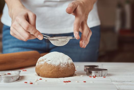 Woman sprinkling flour over fresh dough on kitchen table