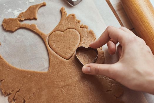 Making gingerbread cookies in shape of a heart for Valentines Day. Woman hand use cookie cutter. Holiday food concept